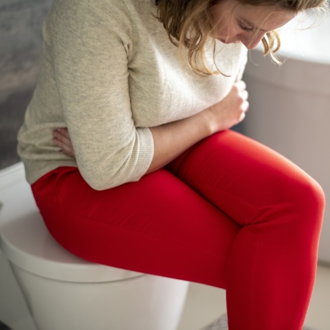 Γυναίκα που πιάνει χαμηλά την κοιλιά της ενώ είναι καθισμένη στη λεκάνη τουαλέτας