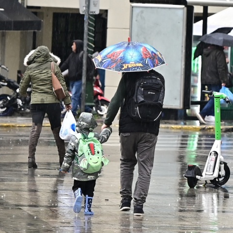 Πατέρας και γιος περπατούν στην Αθήνα εν μέσω βροχής 