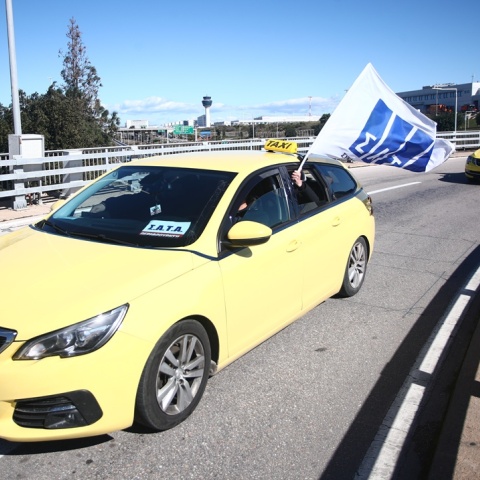 Οδηγός ταξί που οδηγεί και κρατά πανό με το λογότυπο του ΣΑΤΑ