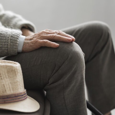 Ηλικιωμένος με καπέλο ακουμπισμένο στο πόδι κάθεται σε καναπέ