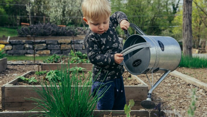 Παιδάκι με ποτιστήρι ρίχνει νερό σε φυτά που βρίσκονται σε παρτέρια