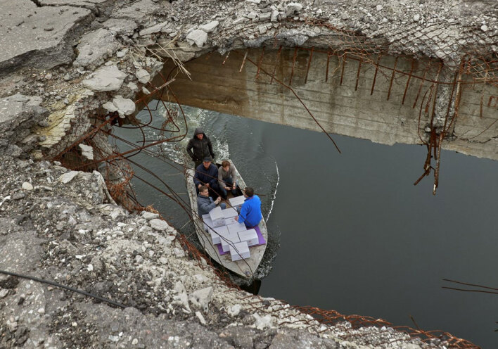 Στην Ουκρανία μέλη του Ερυθρού Σταυρού μεταφέρουν ανθρωπιστική βοήθεια, περνώντας με βάρκα κάτω από βομβαρδισμένη γέφυρα στο Χάρκοβο