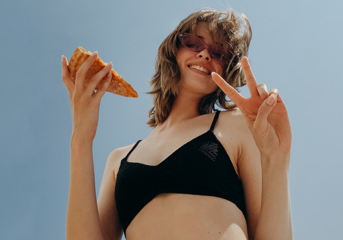 Κοπέλα με γυαλιά ηλίου κρατάει κομμάτι πίτσας