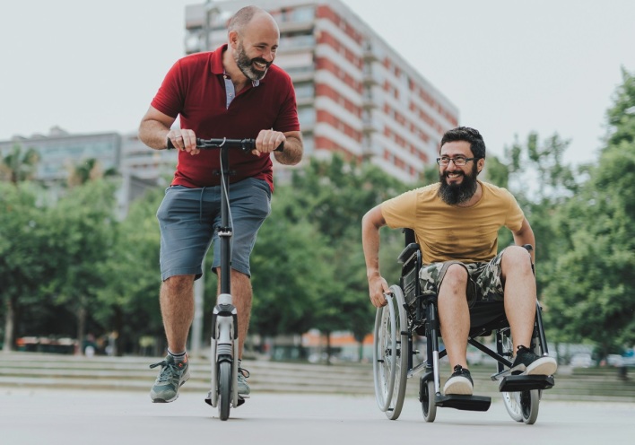 Άνδρας με πατίνι και άνδρας σε αναπηρικό αμαξίδιο