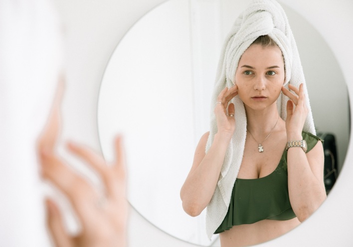 Κοπέλα κοιτάζεται σε καθρέφτη και ακουμπάει το πρόσωπό της