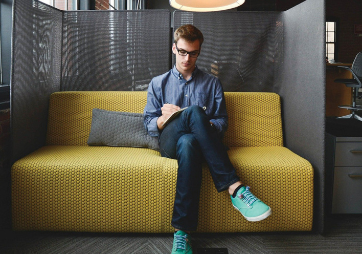 Νεαρός άντρας στον καναπέ εταιρείας, κρατάει σημειώσεις