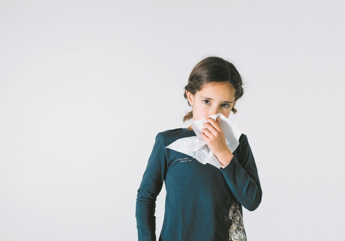 Ένα παιδί κρατάει ένα χαρτομάντηλο και κοιτάει την κάμερα. 