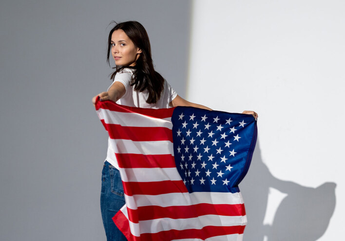 Γυναίκα με λευκό μπλουζάκι και τζιν, που κρατάει την αμερικάνικη σημαία