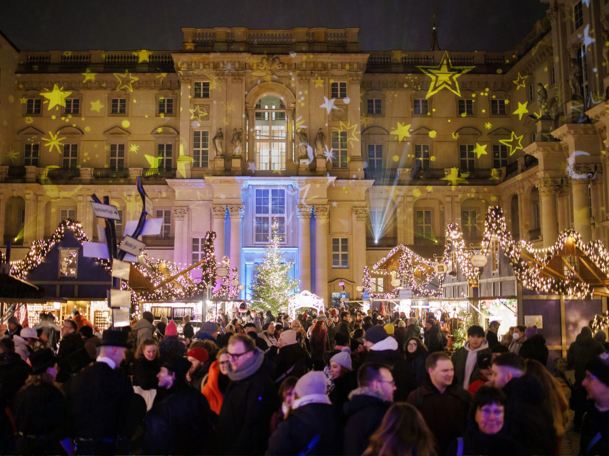 Οι επισκέπτες στέκονται μέσα στη φωτισμένη αυλή κατά τη διάρκεια της χειμερινής αγοράς στο Χούμπολτ του Βερολίνου στη Γερμανία