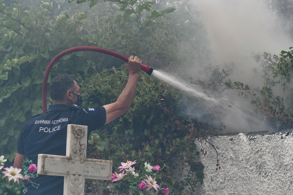 Αστυνομικός επιχειρεί να σβήσει τις φωτιές που έχουν κυκλώσει το νεκροταφείο στην περιοχή Αφίδνες, στη Βόρεια Αττική. 