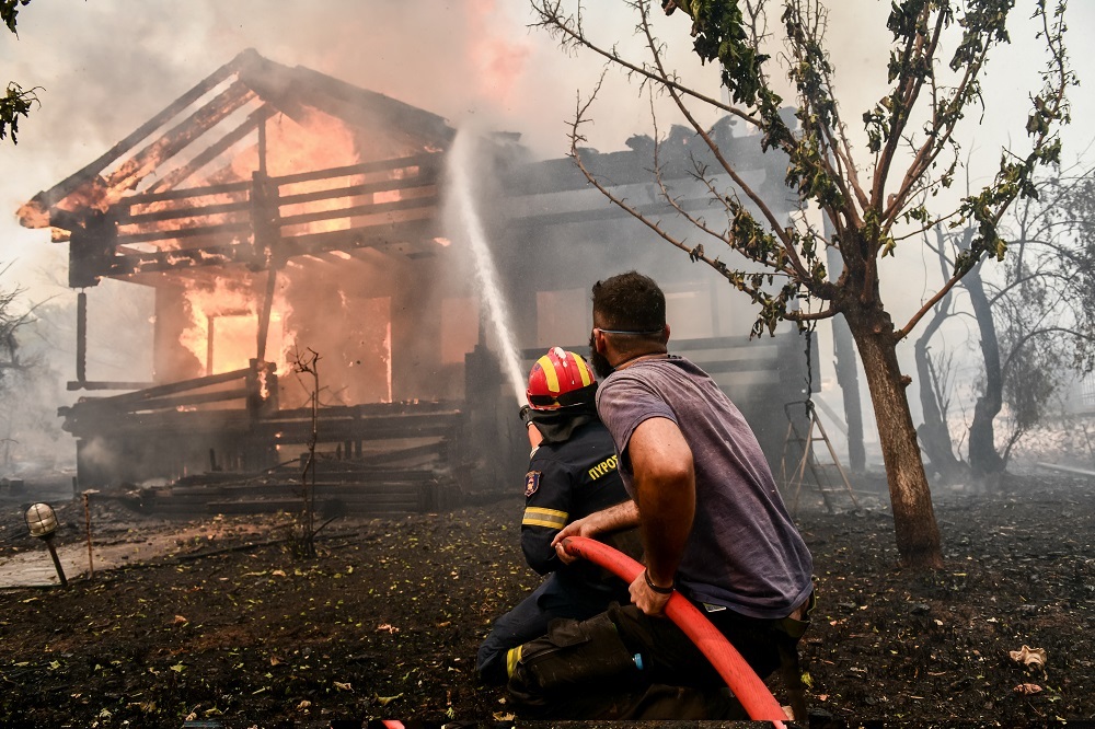 Ένας πυροσβέστης και ένας εθελοντής επιχειρούν να σβήσουν τη φωτιά που κατακαίει ένα σπίτι στις Αφίδνες, στην Βόρεια Αττική. 