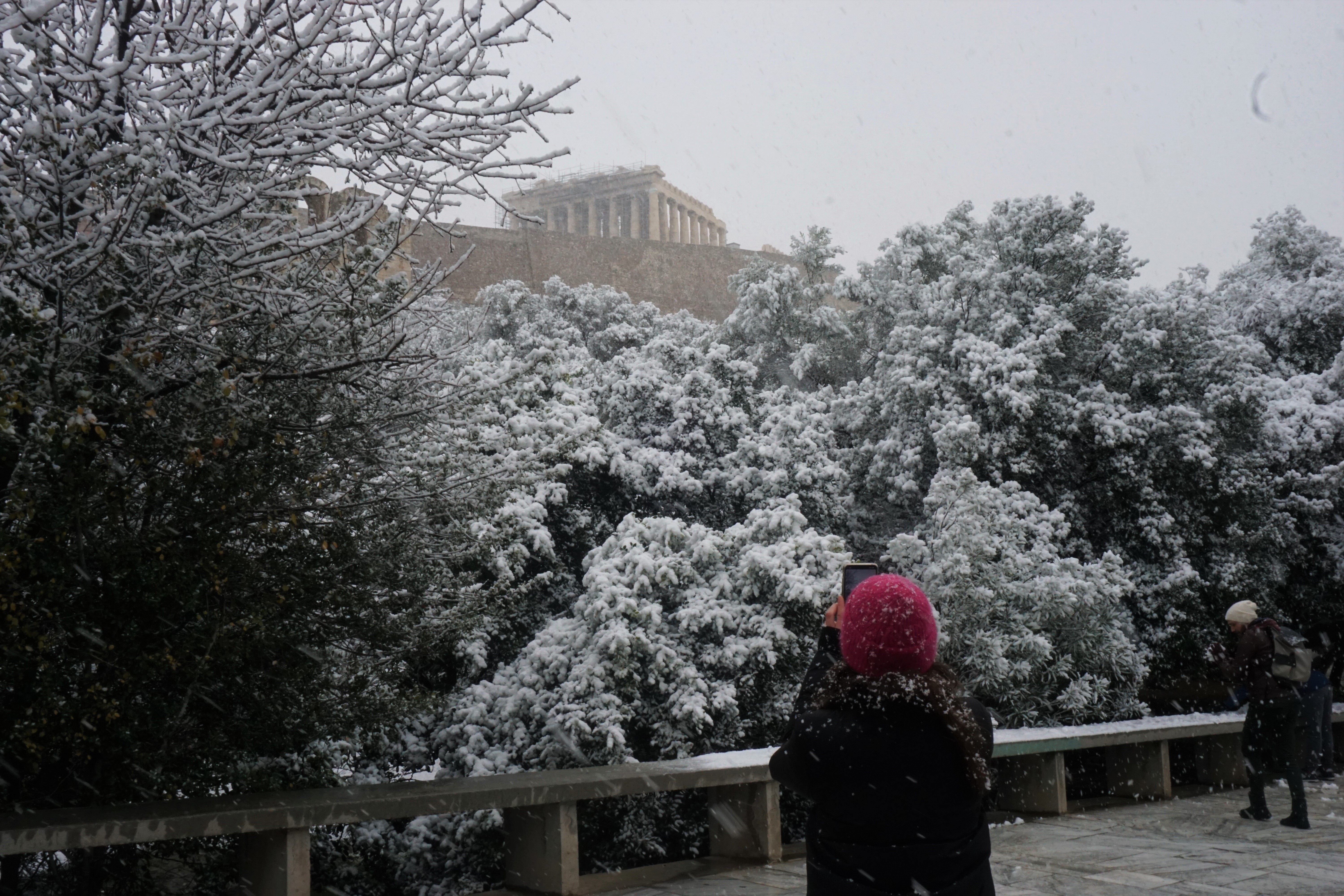 Μια γυναίκα τραβάει φωτογραφία την χιονισμένη Ακρόπολη.