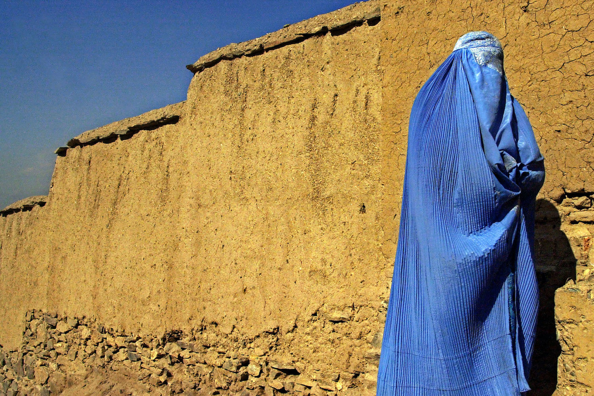 Δημήτρης Μεσσήνης Έξω από τον γιγαντιαίο τοίχο από λάσπη του τάφου του Μογγόλου αυτοκράτορα Babur, μια γυναίκα ντυμένη με ανοιχτή μπλε μπούρκα περιμένει την οικογένειά της να φτάσει στην Καμπούλ, Αφγανιστάν, 2 Νοεμβρίου 2001. Τα αεροπλάνα των Η.Π.Α. βομβάρδισαν σφοδρά την πρώτη γραμμή των Ταλιμπάν βόρεια της Καμπούλ. Έκθεση Δύναμη και οδύνη στο Αφγανιστάν: το καθεστώς Ταλιμπάν 1996-2001 Δημήτρης Μεσσήνης, Πολυχώρος Πολιτισμού Ισλαχανέ – Πρώην Σχολή Τεχνών και Επαγγελμάτων Χαμιδιέ