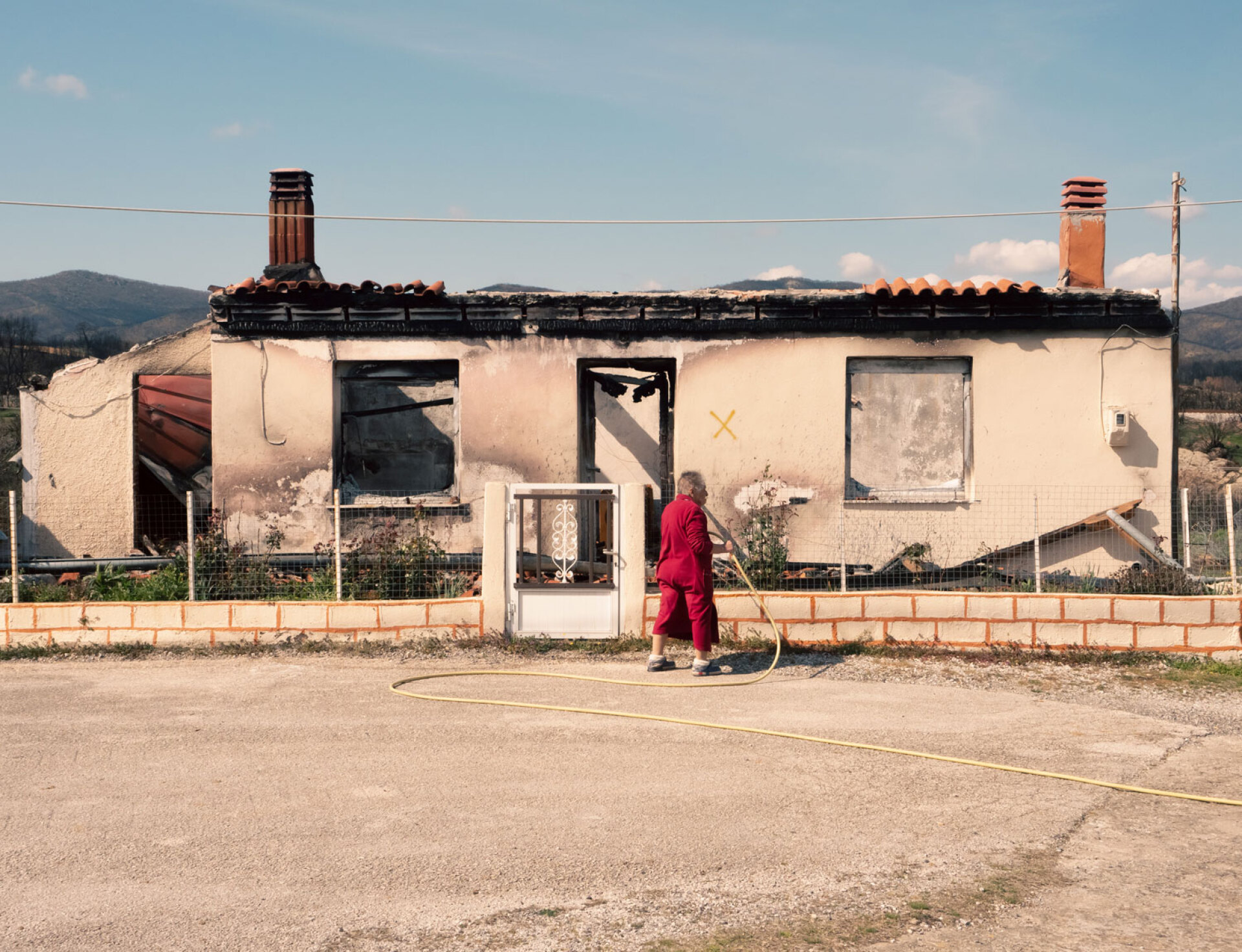 Η 80χρονη κυρία Ζωή Καραβασίλη ποτίζει τις τριανταφυλλιές στον κήπο του καμένου σπιτιού της