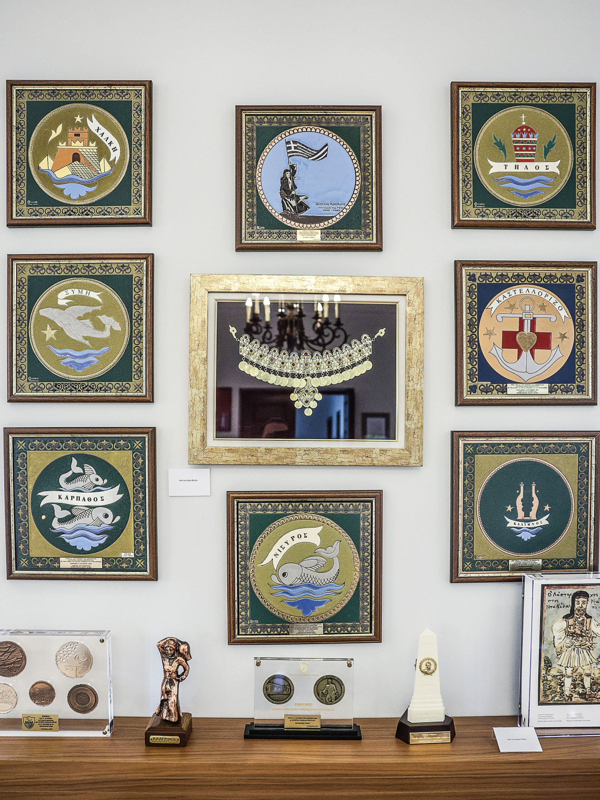 Tα εμβλήματα των νησιών του συμπλέγματος των Δωδεκανήσων. Στην κορυφή η Δέσποινα Αχλαδιώτη, η κυρά της Ρω, που αναπαρίσταται να υψώνει την ελληνική σημαία στην ακριτική νησίδα της Ρω, από το 1943 ως τον θάνατό της, το 1982