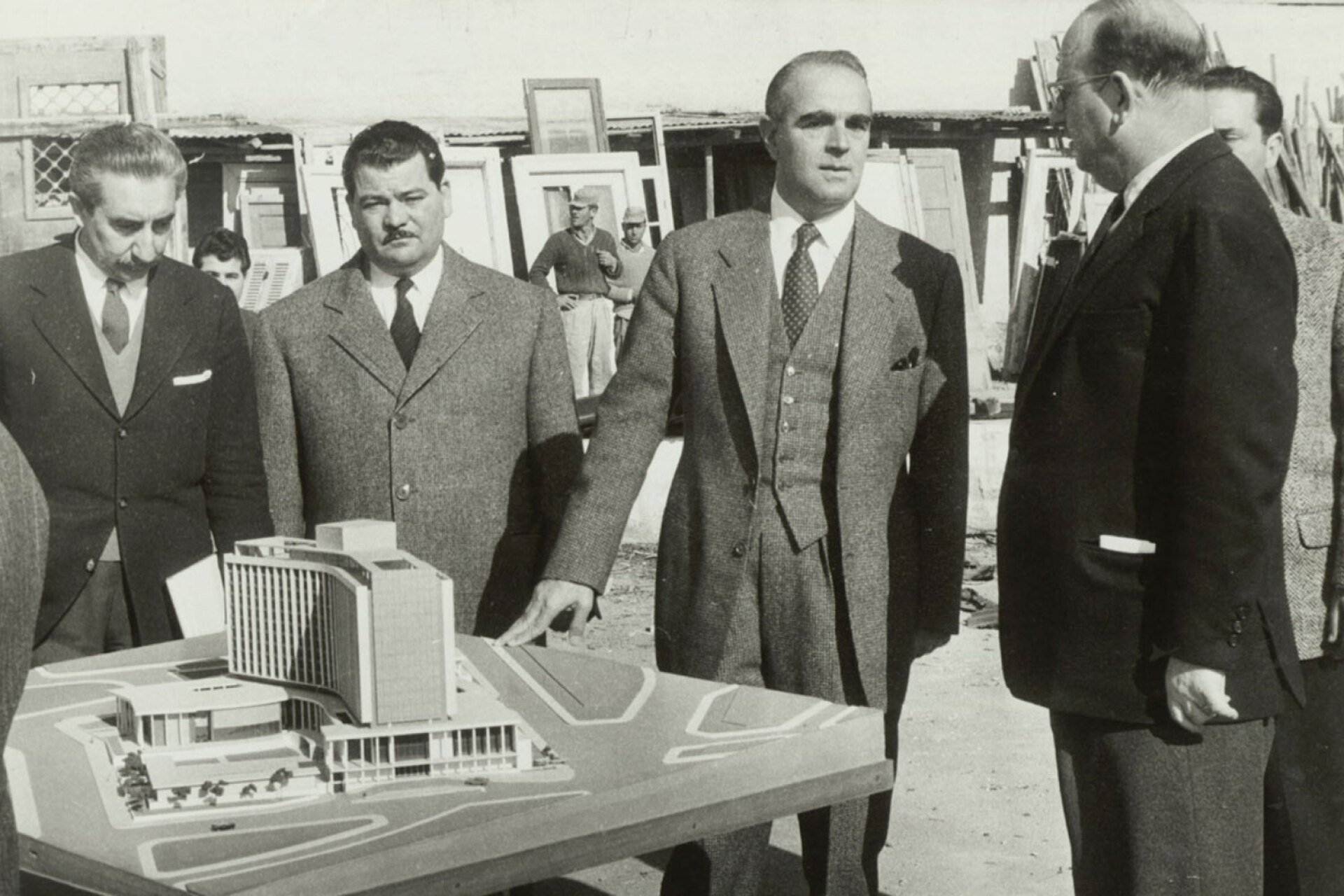 Ο Κωνσταντίνος Καραμανλής, συνοδευόμενος από τον υπουργό Προεδρίας της Κυβέρνησης Κωνσταντίνο Τσάτσο, τον υπουργό Συγκοινωνιών & Δημοσίων Έργων Σόλωνα Γκίκα και τον υφυπουργό Οικισμού Μανώλη Κεφαλογιάννη, επισκέπτεται το εργοτάξιο και την εκσκαφή του γηπέδου, όπου επρόκειτο να ανεγερθεί το ξενοδοχείο Χίλτον, 1959. Η αρχιτεκτονική μελέτη ανατέθηκε το 1958 στους Έλληνες αρχιτέκτονες Προκόπη Βασιλειάδη, Μανώλη Βουρέκα και Σπύρο Στάϊκο