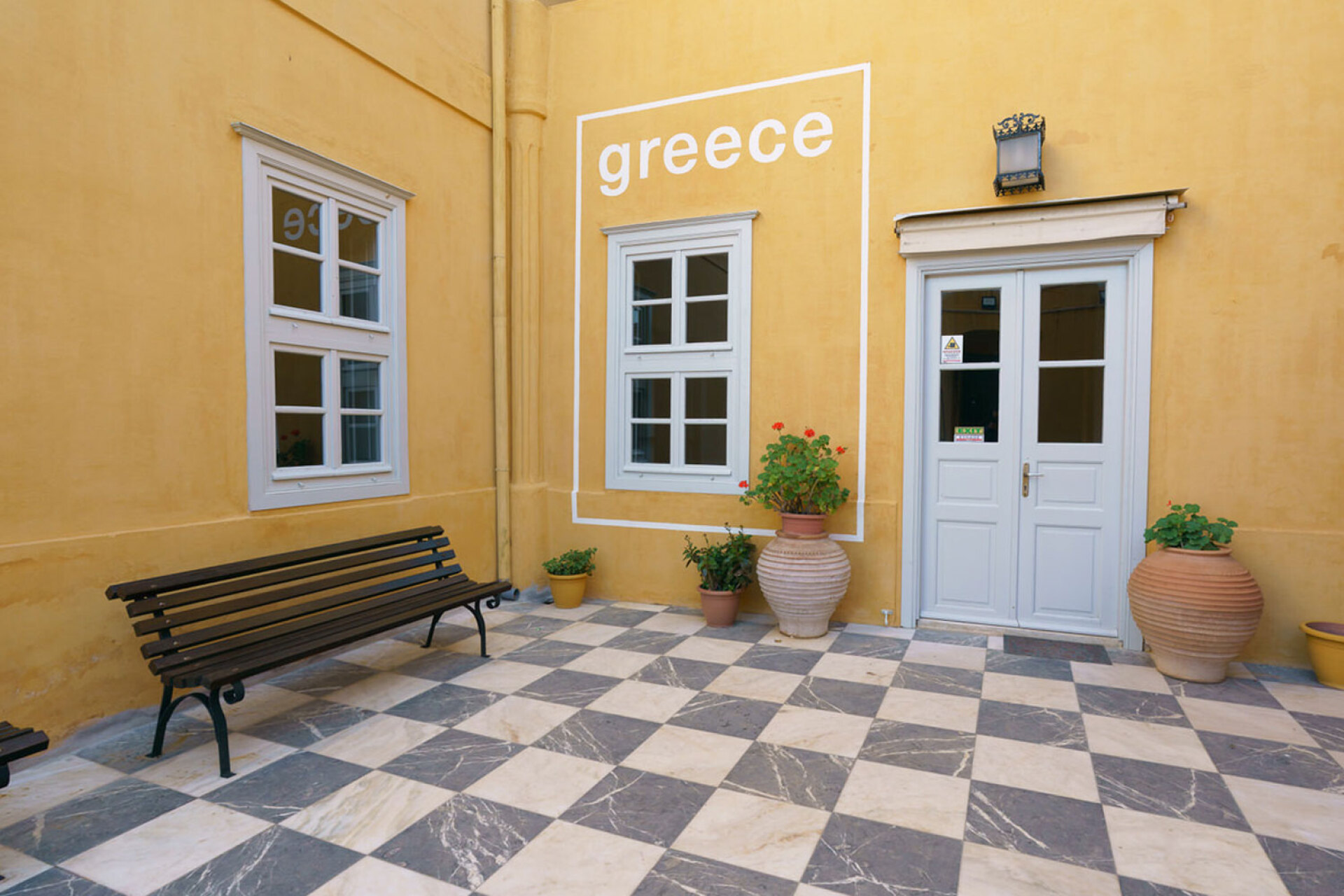 Κεντρική αυλή της Ιστορικής Οικίας Λαζάρου Κουντουριώτη με την τοιχογραφία που μετατρέπει παράθυρο της κεντρικής αυλής της Ιστορικής Οικίας Λαζάρου Κουντουριώτη σε τουριστική αφίσα