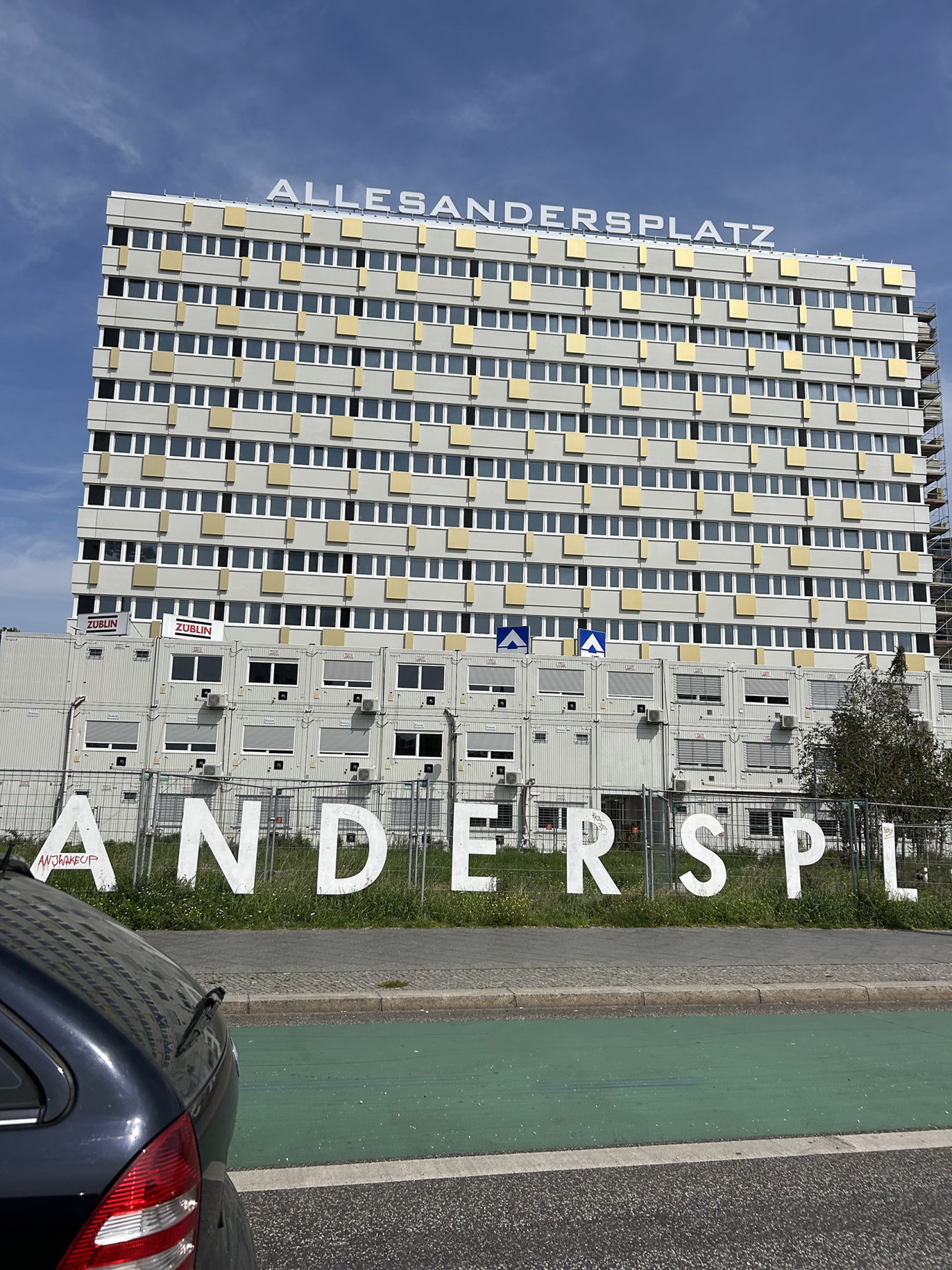 Τυπικά κτίρια γραφείων/κατοικιών της DDR. Το λογοπαίγνιο Allesandersplatz είναι σύγχρονη καλλιτεχνική/αστική παρέμβαση που παίζει με το όνομα της πλατείας (Alexanderplatz → Alles anders Platz = «όλα διαφορετικά μέρος»)