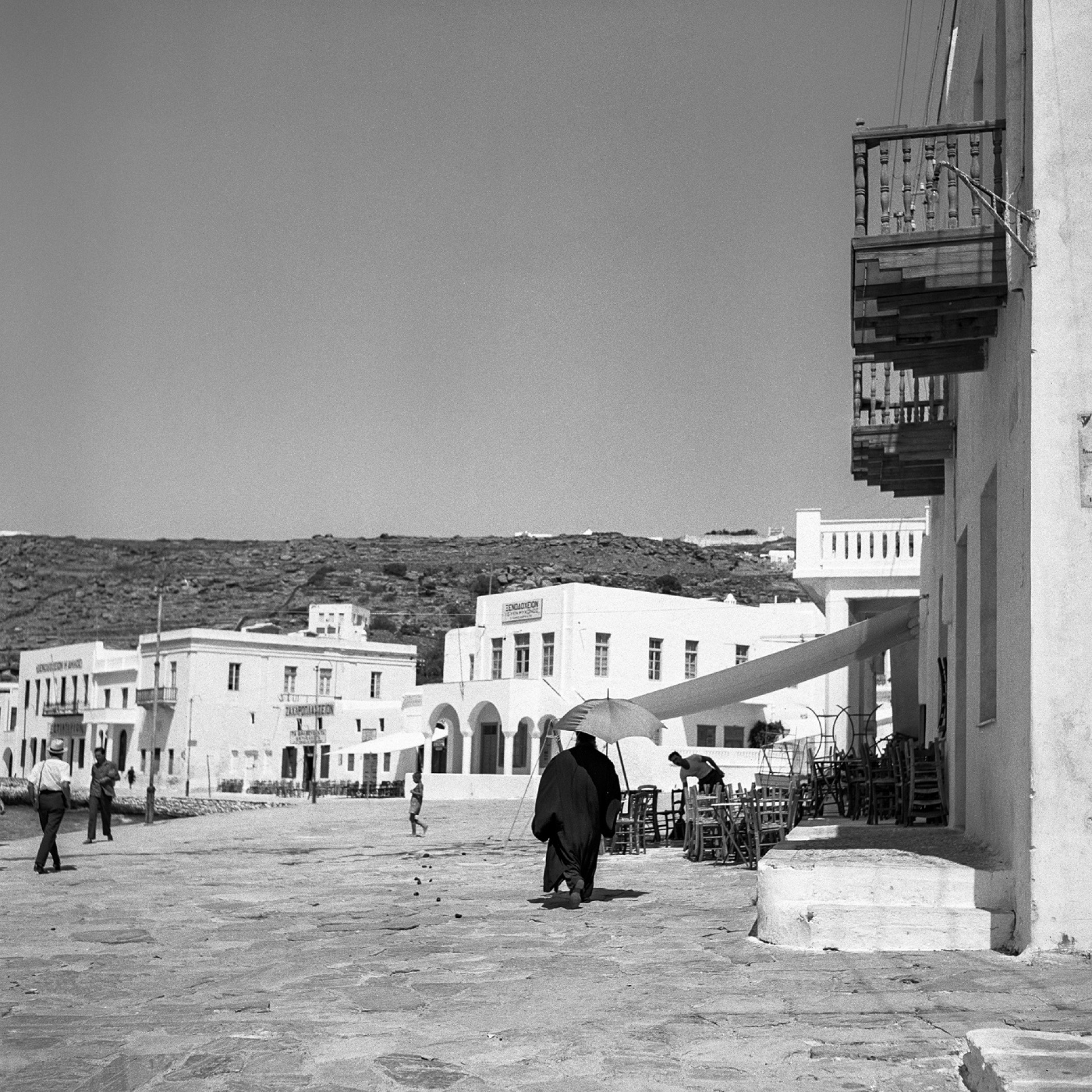 Μύκονος. Man with umbrella: Στην παραλία, στην πλατεία Μαντώς Μαυρογένους. ©Robert McCabe
