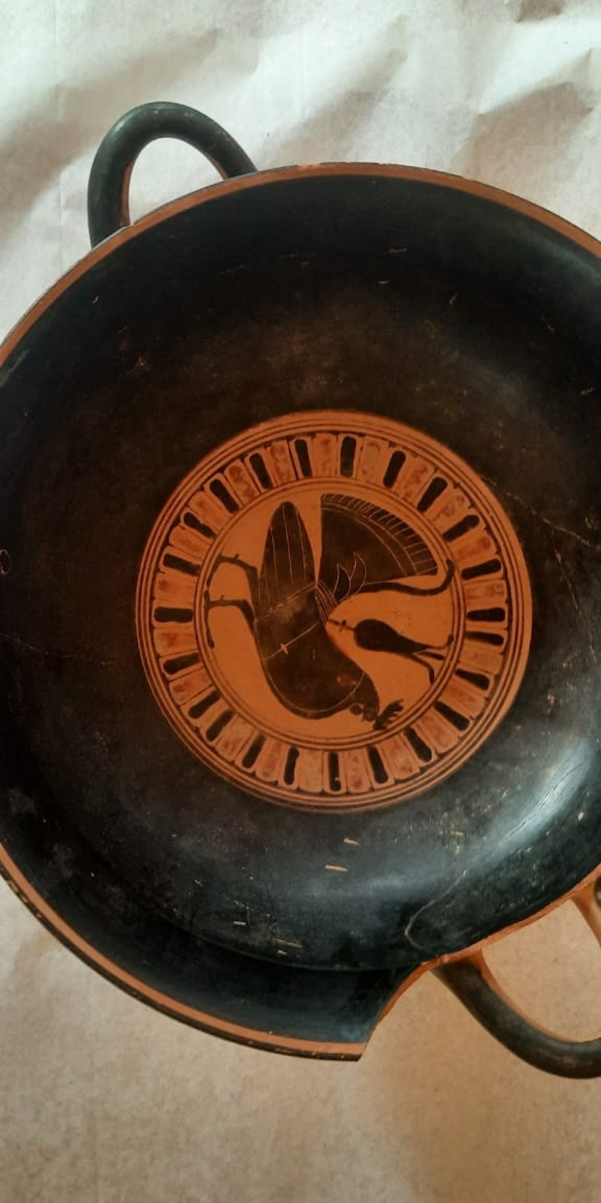 Μελανόμορφη κύλικα τύπου Σιάννων με παράσταση πυγμάχων παρουσία κριτών. Στον τόντο απεικονίζεται κόκορας. Γύρω στα μέσα του 6ου αι. π.Χ.