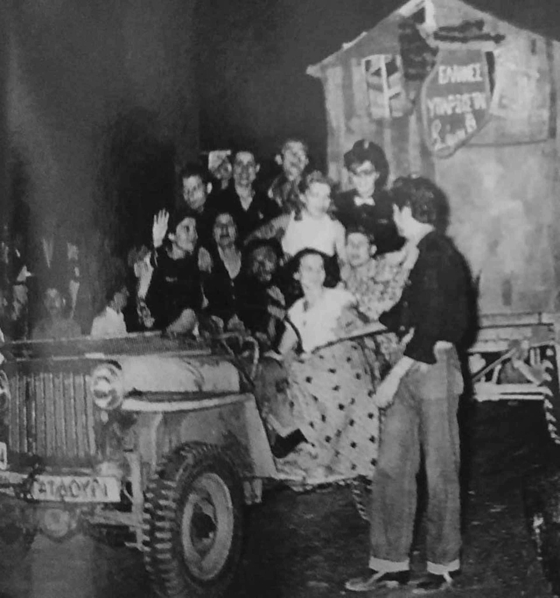 Το τζιπ του Σίμου, το «Ιπτάμενο Γαϊδούρι», με ομοίωμα της «Ιπτάμενης Παράγκας», ρυμουλκούμενο σε πλατφόρμα. Ο Κουτρουμπούσης με ψηλό καπέλο, 1953.