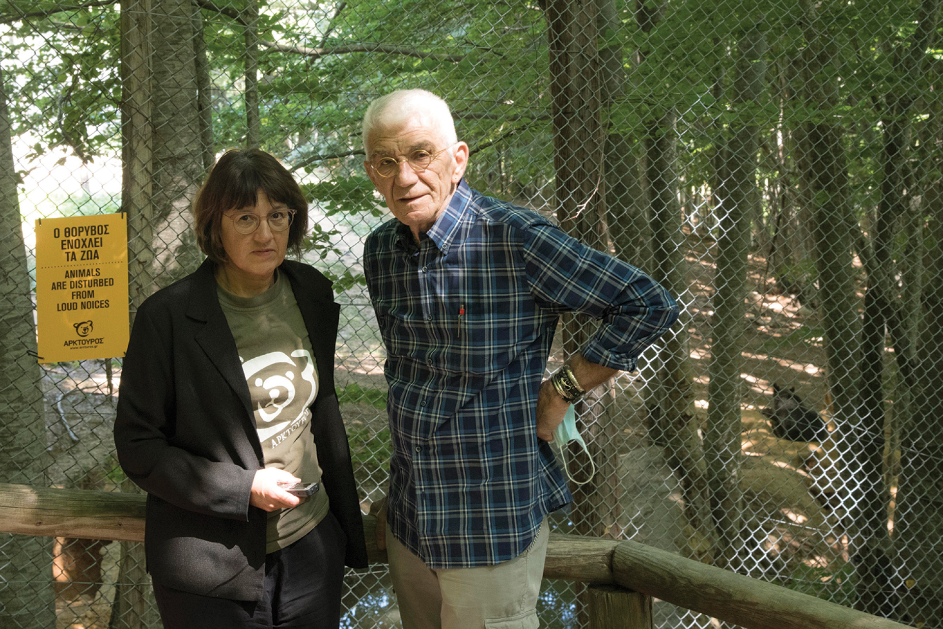 Ο Γιάννης Μπουτάρης στο καταφύγιο άγριων ζώων του Αρκτούρου στο Νυμφαίο με τη συγγραφέα Μαρία Μαυρικάκη. Πίσω τους διακρίνεται η Βαρβάρα, η αρκούδα που είναι υιοθετημένη από τον Πατριάρχη. ©Βαγγέλης Τσιάμης