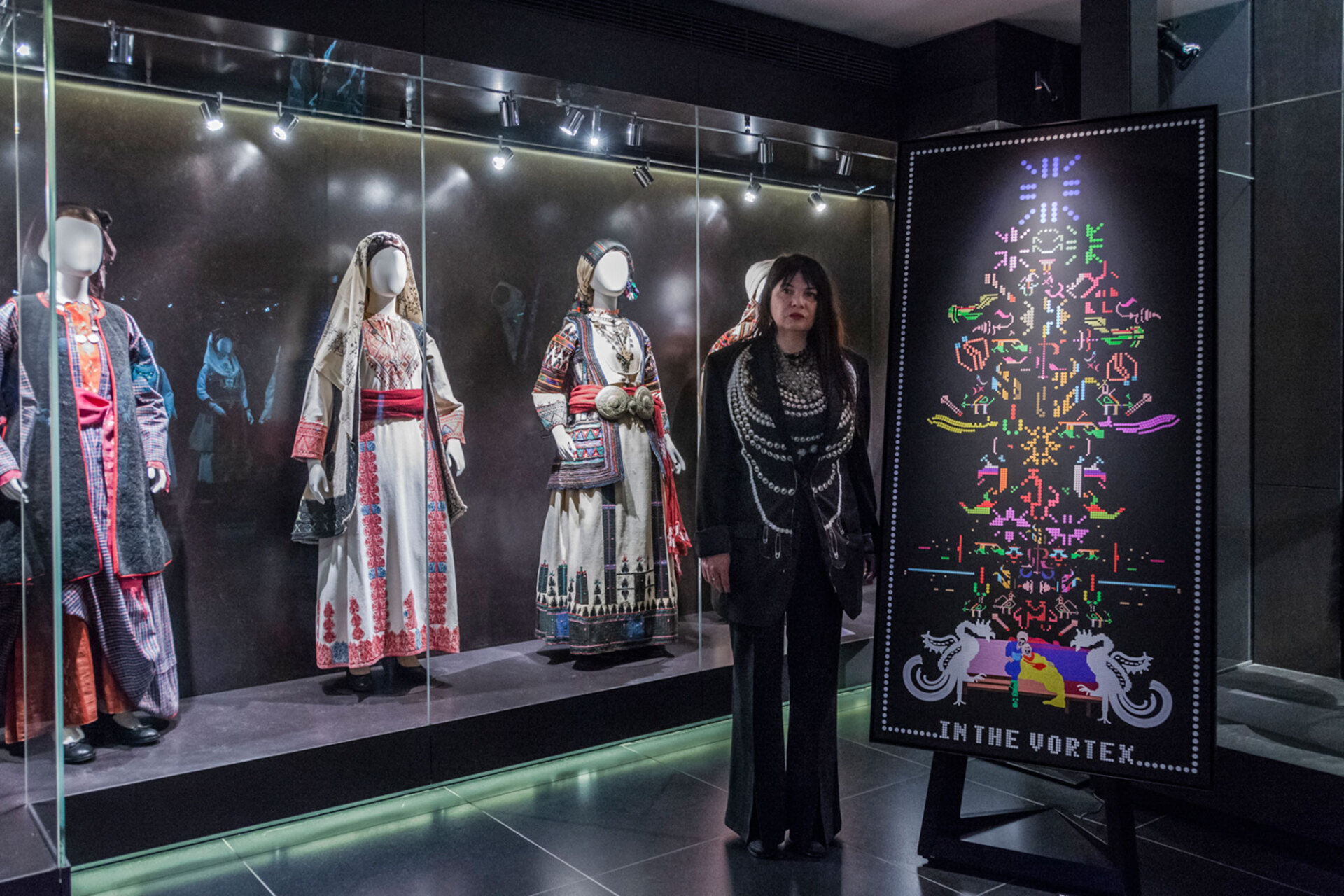 Η Μαρία Όλγα Βλάχου δίπλα στο έργο της με φόντο ένα μέρος της συλλογής Καρέλια