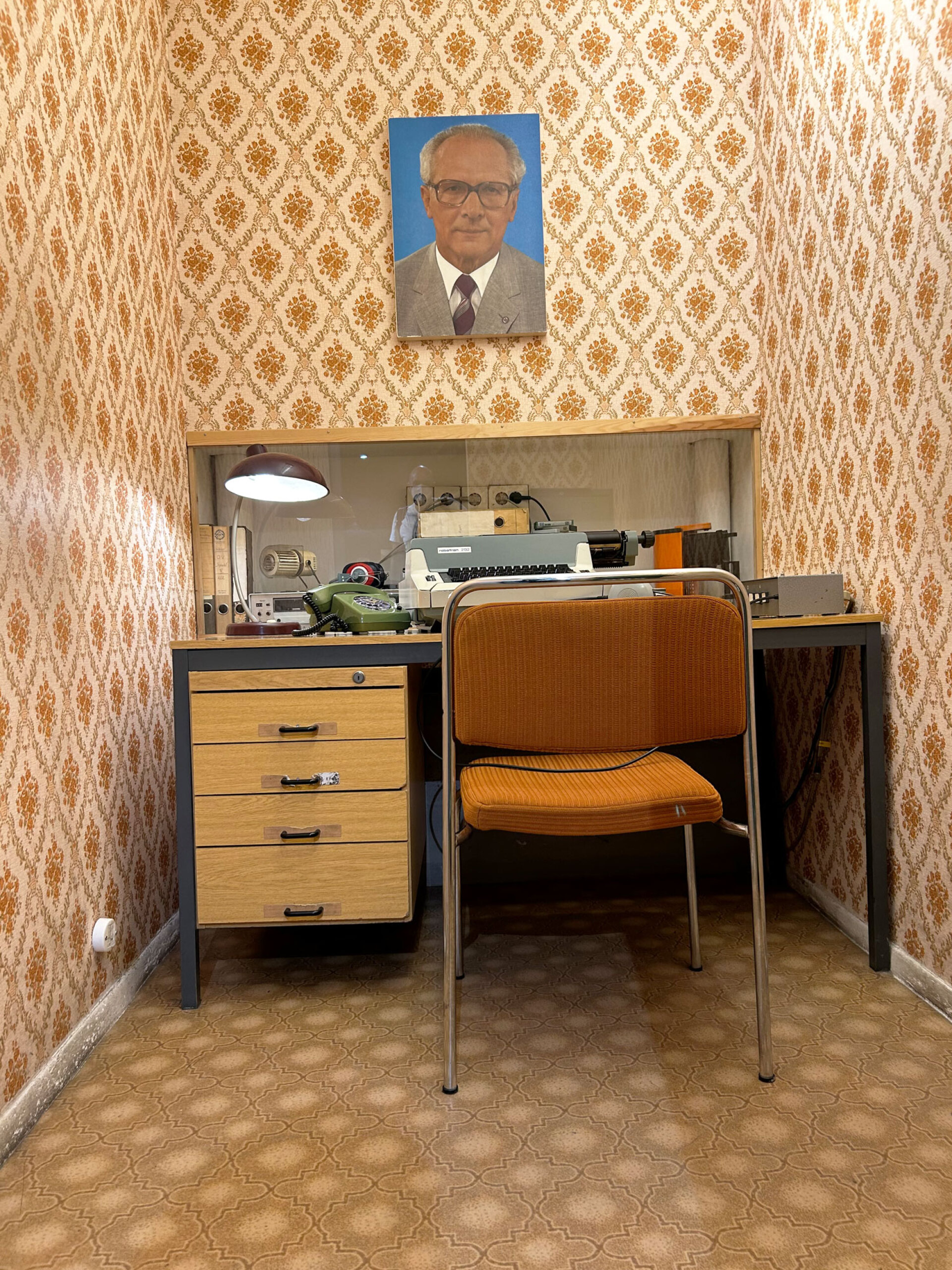 Γραφείο της Stasi, γραφομηχανή, ταπετσαρία και το βλέμμα του Χόνεκερ από πάνω. Ένα σκηνικό που θυμίζει πως στην DDR η παρακολούθηση ήταν κομμάτι της καθημερινότητας