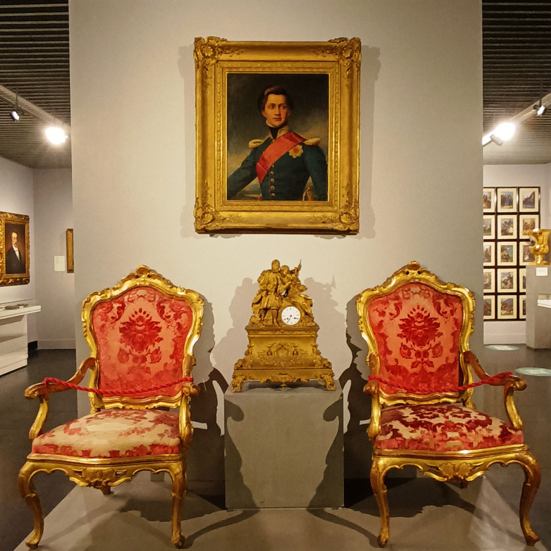 Δύο πολυθρόνες από το υδραϊκό αρχοντικό του Βούλγαρη που είχαν μεταφερθεί στο Ναύπλιο για την εκεί υποδοχή του Όθωνα, στις 25 Ιανουαρίου 1833 | Ανάμεσά τους, ένα επιχρυσωμένο επιτραπέζιο ρολόϊ γαλλικής κατασκευής και φιλελληνικής εμπνεύσεως, και από πάνω η προσωπογραφία του Όθωνα, έργο του Γιόζεφ Καρλ Στίλερ