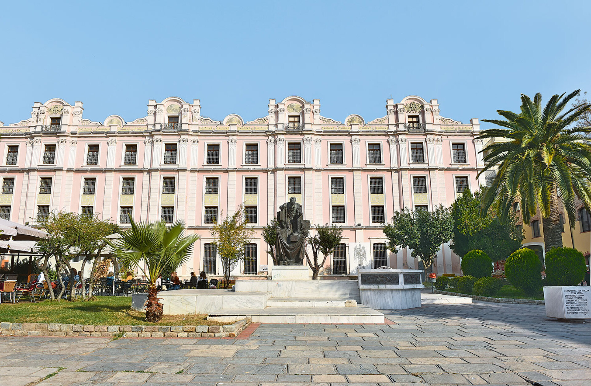 Η Πλατεία Καπνεργάτη με το ομώνυμο μνημείο, όπως διαμορφώθηκε το 1986. Στο βάθρο το σύμπλεγμα των τριών καπνεργατών, στο ημικυκλικό μαρμάρινο τοιχίο οι ένθετες χάλκινες συνθέσεις με τα χέρια που επεξεργάζονται καπνόφυλλα, και στην άκρη δεξιά ο μαρμάρινος αναθηματικός κύβος με τα ονόματα των πεσόντων καπνεργατών. Στο φόντο η Δημοτική Καπναποθήκη που αναμένεται να στεγάσει το Μουσείο Καπνού. Φωτογραφία Μ. Παυλίδης, συλλογή Μ. Κριθαρέλλη.