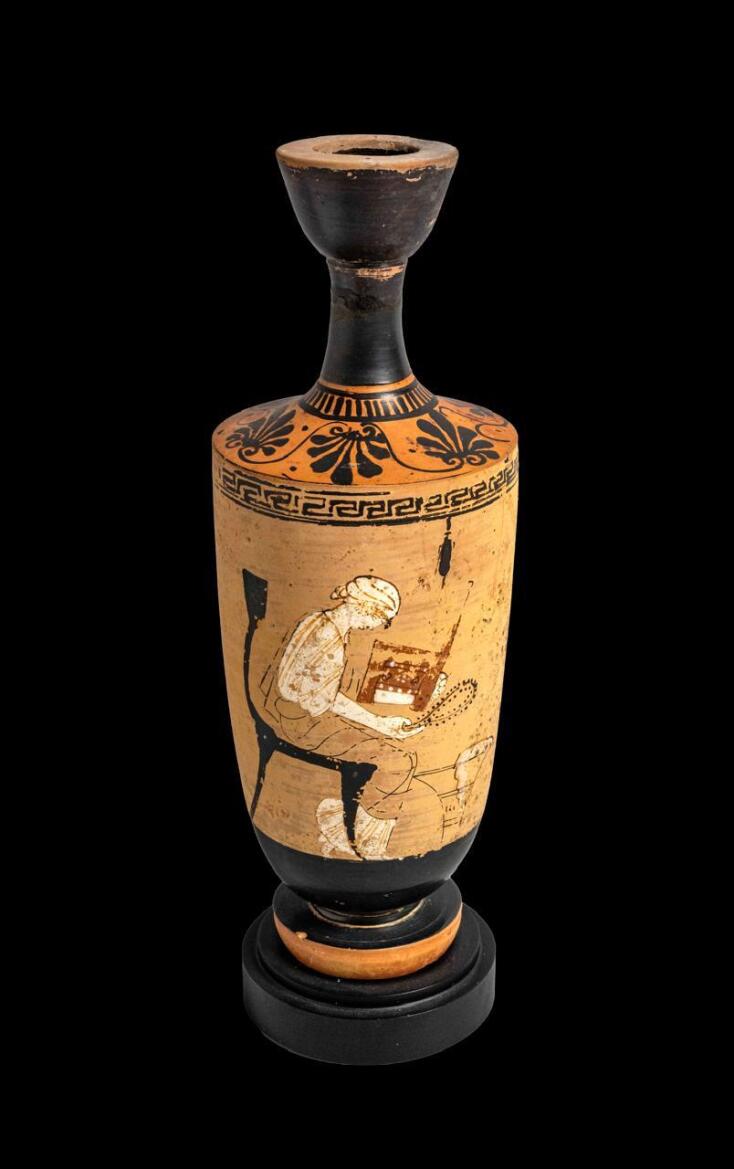 Αττική λήκυθος. Παριστάνεται καθισμένη σε κλισμό γυναικεία μορφή που κρατά κάτοπτρο και πυξίδα για κοσμήματα. Αποδίδεται στον «Ζωγράφο των Αθηνών 1826».