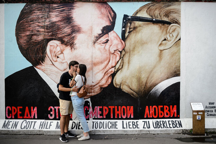 Ζευγάρι φιλιέται μπροστά στο γκράφιτι του Ντμίτρι Βρούμπελ με το φιλί Μπρέζνιεφ και Χόνεκερ στο Τείχος του Βερολίνου
