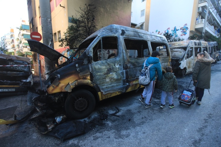 Μητέρα με το παιδί της περπατούν μπροστά από το καμένο αυτοκίνητο στου Ζωγράφου