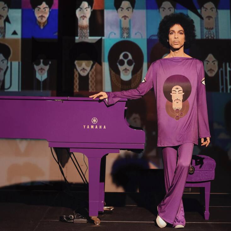Ο Prince ντυμένος στα μωβ δίπλα σε ένα μωβ πιάνο