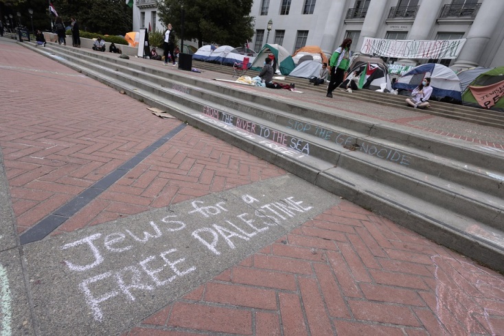 Σύνθημα με κιμωλία στο έδαφος μπροστά από σκαλιά - στο βάθος πανεπιστήμιο με φοιτητές και σκηνές
