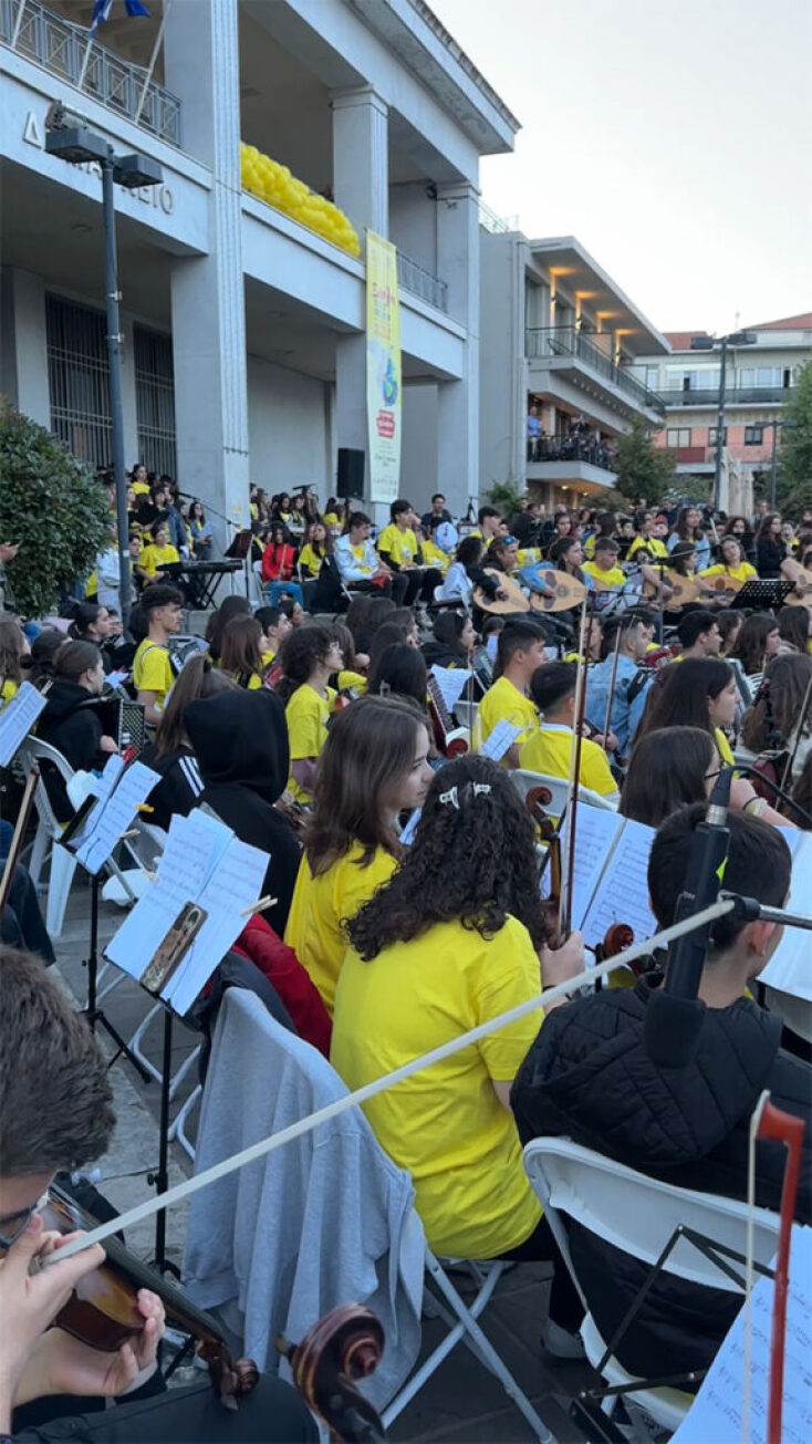 Δεκάδες μαθητές στα κίτρινα κρατάνε μουσικά όργανα καθιστοί