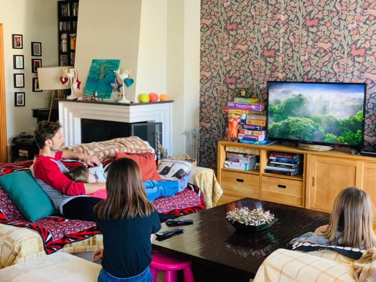 Ο Μάξιμος Μουμούρης και οι κόρες του βλέπουν τηλεόραση στο σαλόνι του σπιτιού τους