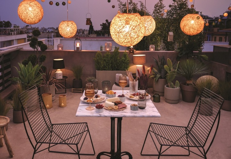 Ταράτσα με καρέκλες, τραπέζι, φωτιστικά, φυτά και πιάτα με φαγητό στο τραπέζι