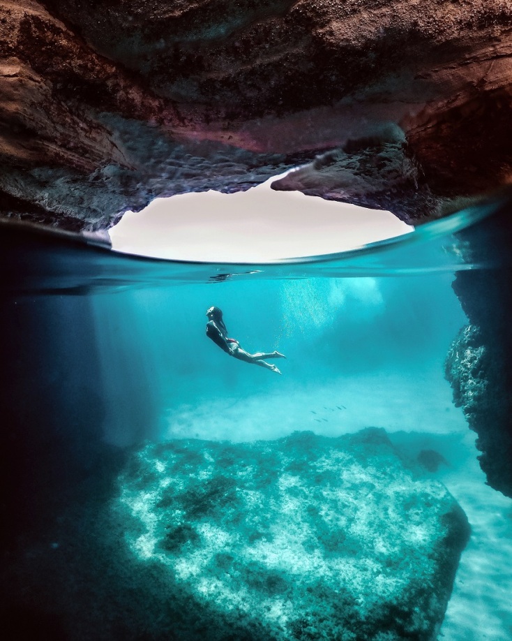 Τοπίο με βράχια και θάλασσα και κοπέλα που κολυμπάει υποβρύχια