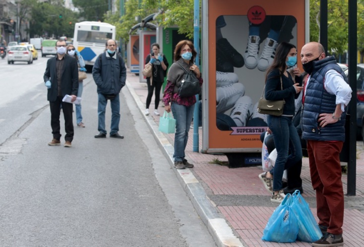 Φορώντας προστατευτική μάσκα, περιμένει σε στάση λεωφορείου