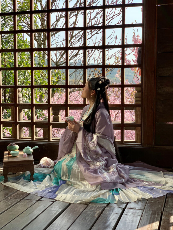 Κινέζα με παραδοσιακή φορεσιά καθισμένη δίπλα σε ξύλινο παράθυρο
