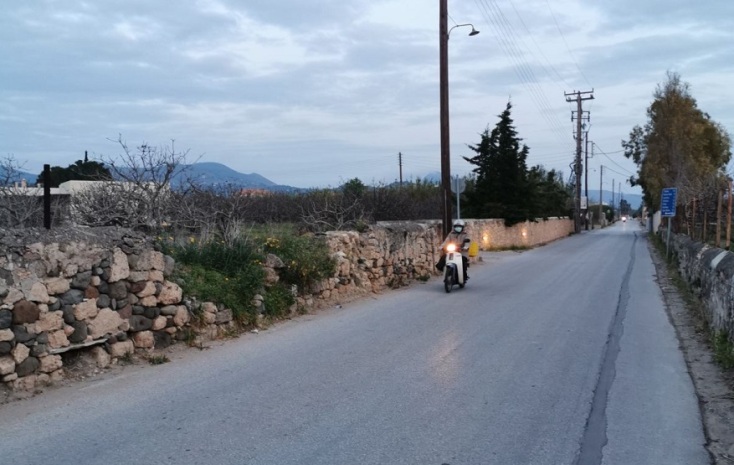 Γυναίκα με μάσκα πάνω σε μηχανάκι σε δρόμο στην Αίγινα