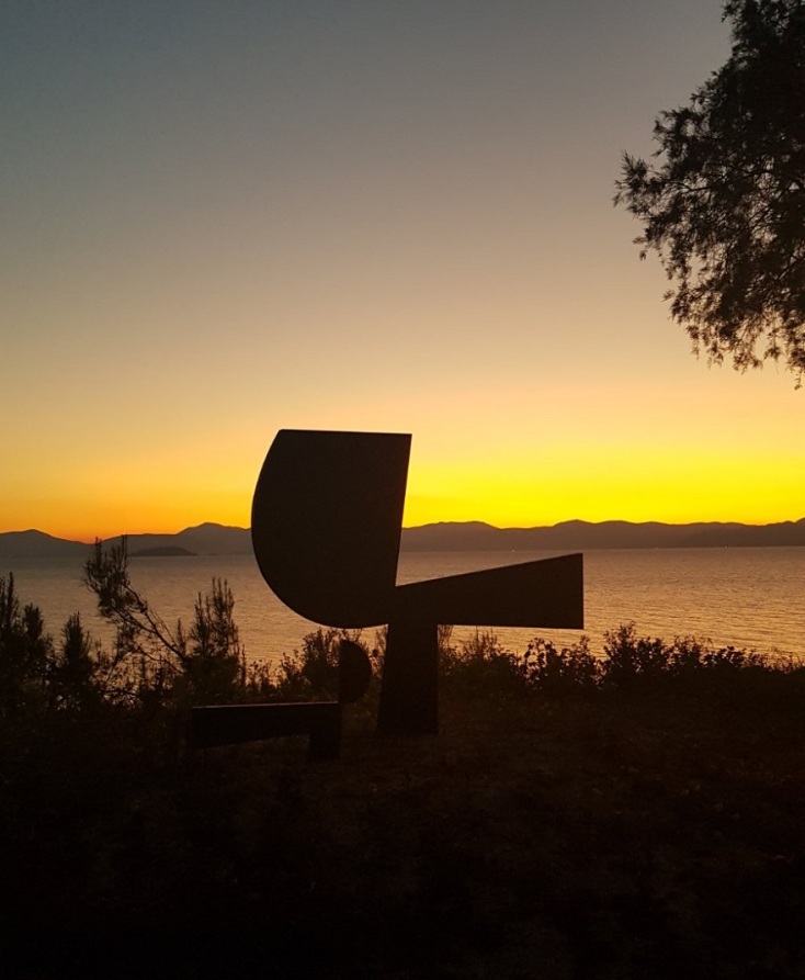 Γλυπτό του Γιάννη Μώραλη στην Αίγινα με φόντο το ηλιοβασίλεμα