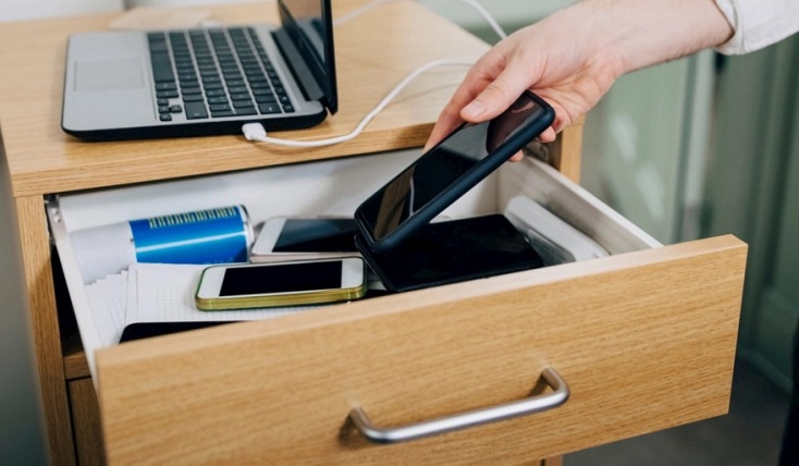 Κομοδίνο με laptop και ανοιγμένο το πρώτο συρτάρι γεμάτο παλιά τηλέφωνα