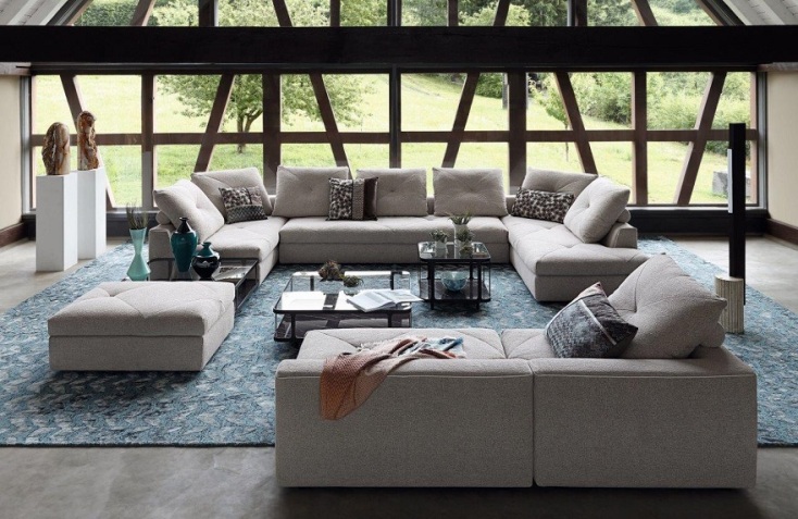 Φωτεινό σαλόνι με μεγάλα παράθυρα, γκρι καναπέ 3 κομματιών, γυάλινα τραπεζάκια σαλονιού, διακοσμητικά και μεγάλο μπλε χαλί