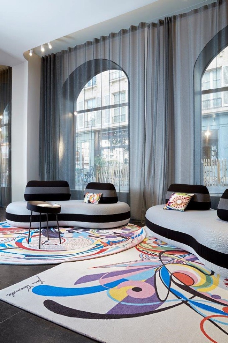 Γκρι καναπέδες με καμπύλες, χαλιά με ποπ σχέδια, μεγάλα παράθυρα και γκρι διάφανες κουρτίνες