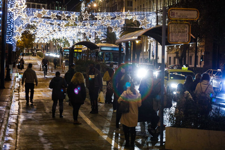 Πολίτες περπατούν στην Πανεπιστημίου ή περιμένουν στη στάση το λεωφορείο με φόντο τον χριστουγεννιάτικο στολισμό
