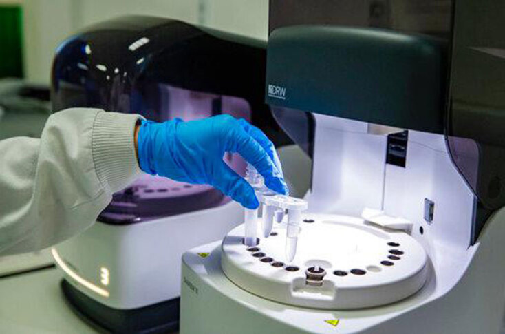 Χέρι με μπλε γάντι ακουμπάει δοκιμαστικό σωλήνα σε δίσκο δειγμάτων χημικού εργαστηρίου