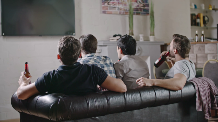 thumbnail_rear-view-of-male-friends-sitting-on-sofa-drinking-beer-and-watching-game-on-tv-then-celebrating-goal-and-hugging_bx5kr8_wl_thumbnail-full01.png