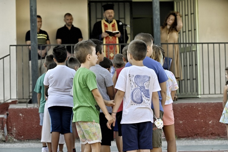 Μαθητές πιασμένοι χέρι χέρι κατά τη διάρκεια του αγιασμού από ιερέα σε προαύλιο σχολείου